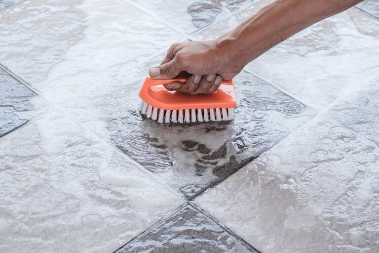 Person scrubbing tile floor with an orange brush